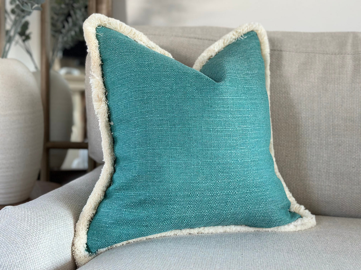 A square textured green blue turquoise cushion with cream fringe trim. Can be placed in living room or bedroom to brighten up decor.