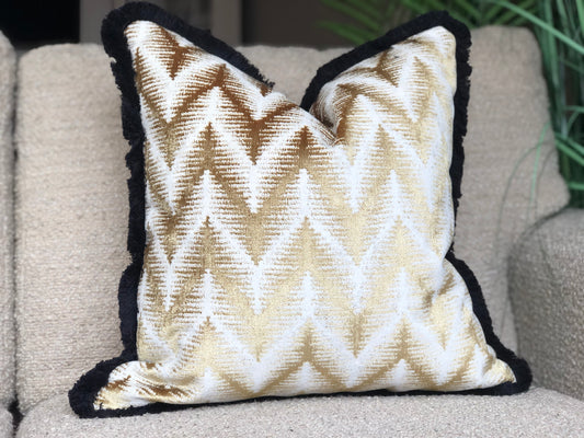 A picture of a good and cream cushion made from velvet with a black fringe trim.