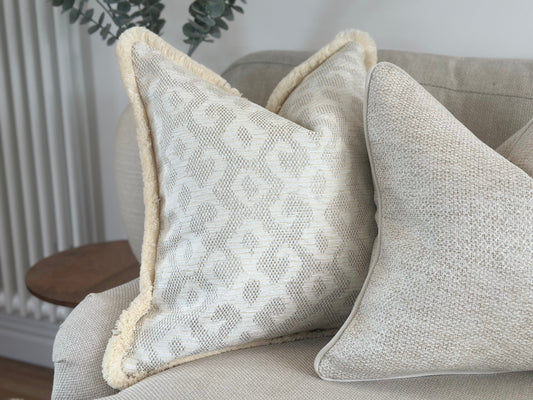 A Luxury high end patterned cushion with fringing in ivory cream.