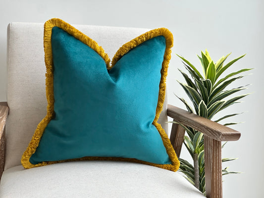 Teal velvet cushion with mustard fringe trim.