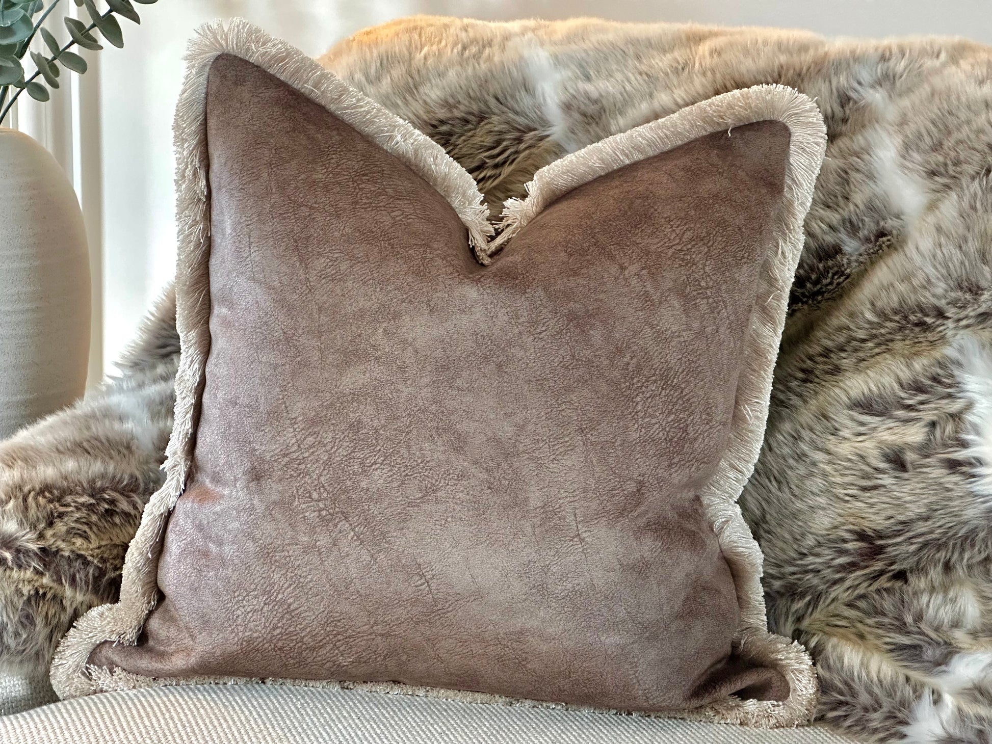 A luxury mocha brown toned cushion with a soft, velvety texture and fringed trim, adding warmth and sophistication to a cosy interior setting.