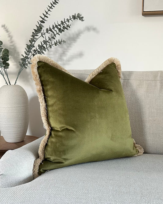 Luxury antique moss green velvet cushion with a fringe trim, perfect for earthy neutral decor trends.