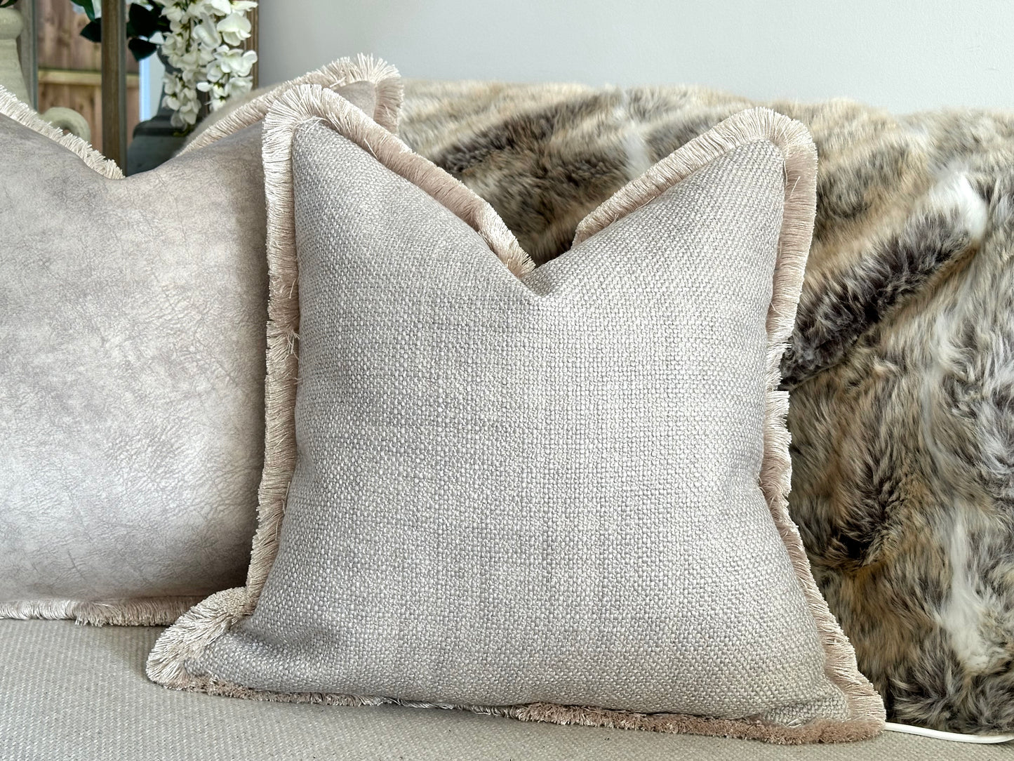 Luxury neutral-toned cushion with a textured woven fabric and elegant fringe trim, adding depth and sophistication to modern and timeless interiors. Perfect for styling on sofas, beds, and accent chairs for a refined, cosy aesthetic