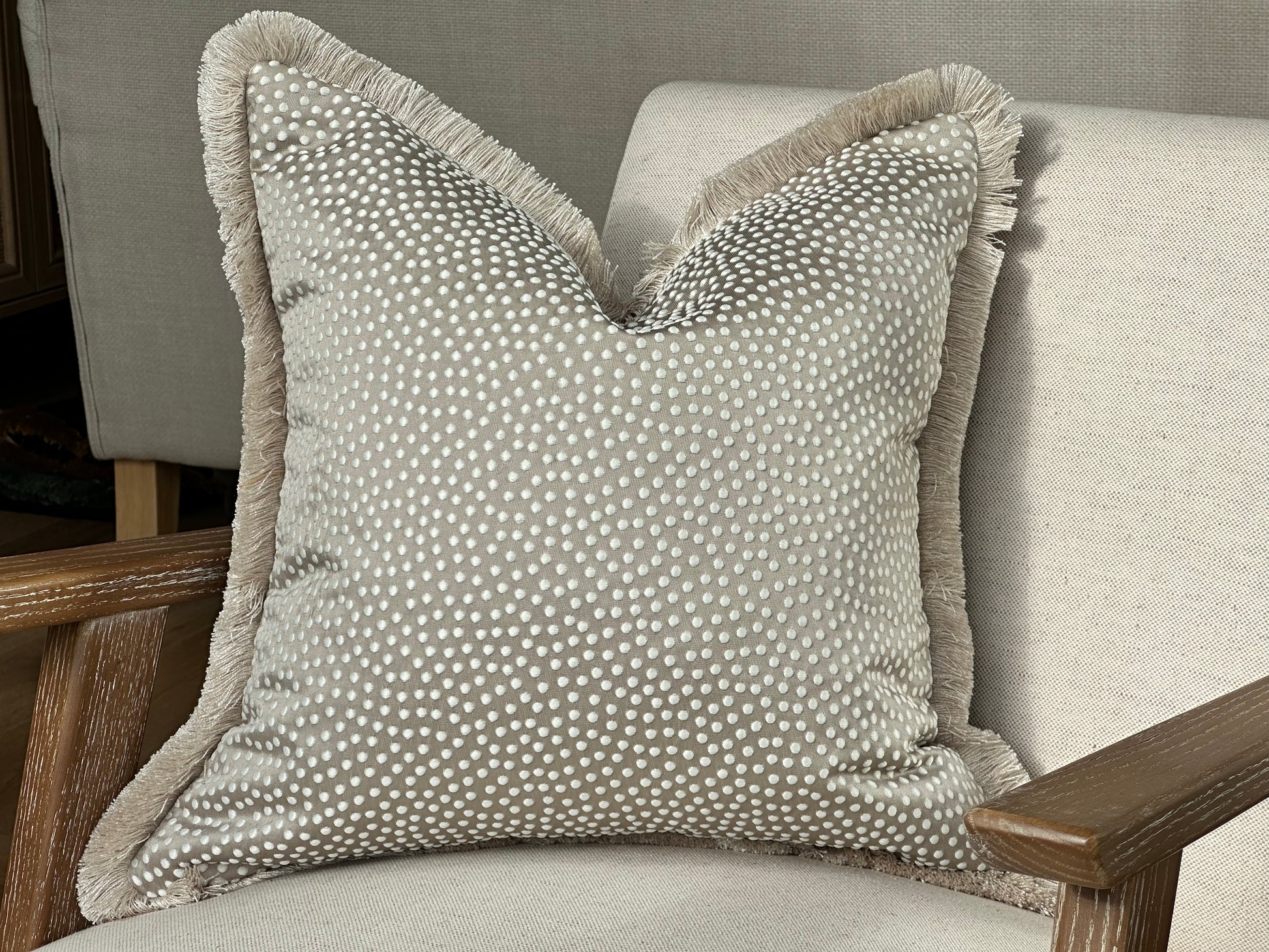 A luxury oyster beige cushion with a white dotted pattern and a soft, fringed trim.
